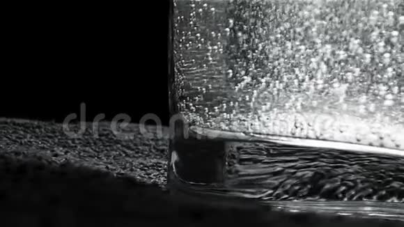 在黑暗的背景上编织的小垫子上站着闪闪发光的水的玻璃特写单色视频的预览图
