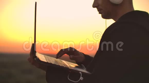 一个男人戴着白色的大耳机手指放在笔记本电脑的键盘上站在大楼的屋顶上视频的预览图
