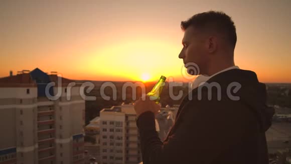 一个人喝着啤酒站在屋顶上沉思世界从高处看日落时的城市景色视频的预览图