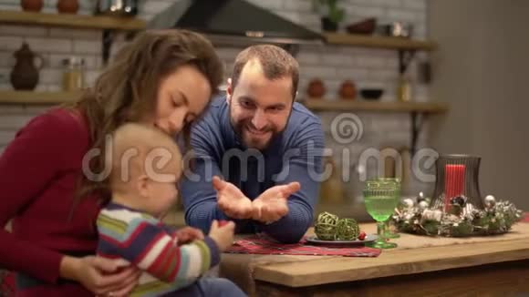 母亲父亲和婴儿在现代厨房里玩得很开心爸爸和妈妈一起玩孩子男人让男孩分享糖果视频的预览图