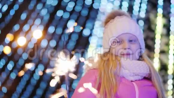 一个女孩在一棵大圣诞树模糊灯光的背景上玩着火花视频的预览图