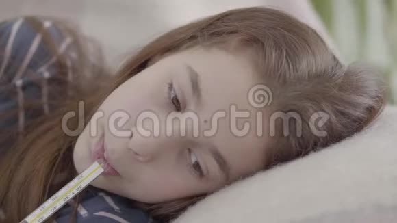 合上躺在床上的悲伤的病女嘴里放着体温计生病孩子的概念医学和健康视频的预览图