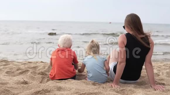 有孩子的女人坐在海滩上看着大海视频的预览图