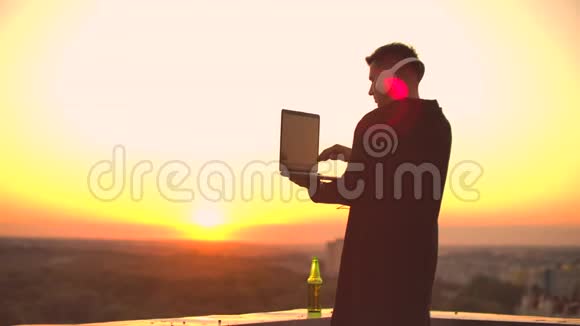 一个人喝着啤酒站在屋顶上沉思世界从高处看日落时的城市景色视频的预览图