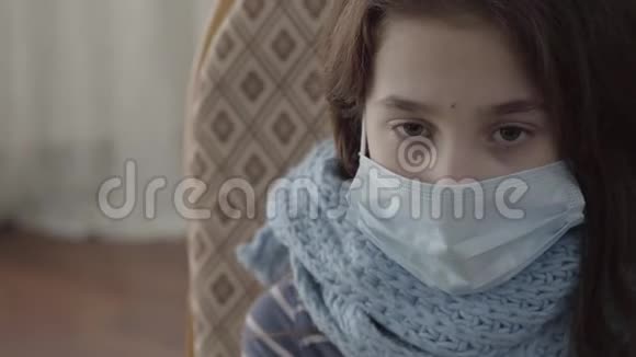 特写肖像悲伤生病的女孩坐在扶手椅上脸上戴着无菌面具在室内患病儿童的概念视频的预览图