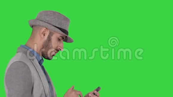 严肃的阿拉伯休闲男子在绿色屏幕上行走时使用智能手机色度键视频的预览图