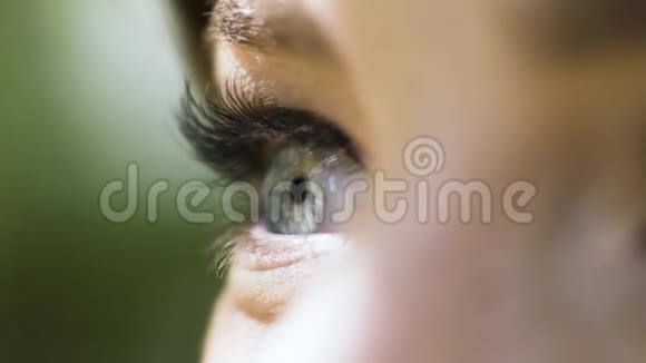 绿色的美丽的女性眼睛在模糊的绿色背景上有长长的睫毛行动闭上女性的眼睛视频的预览图