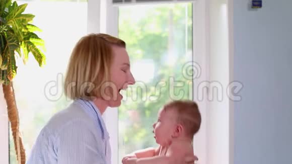 一位慈爱快乐的年轻母亲在托儿所拥抱一个哺乳的儿子很美的光爱家庭和视频的预览图