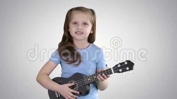 小女孩一边唱着小吉他一边在渐变背景下走向相机视频的预览图