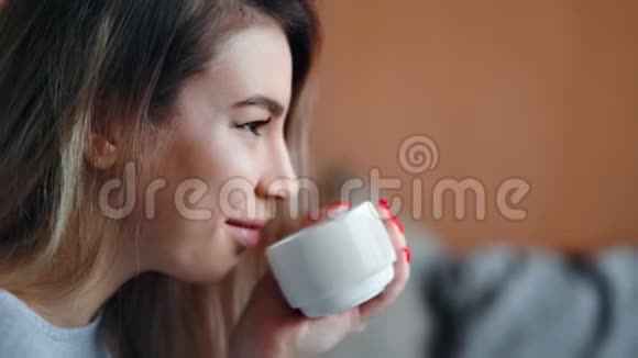 漂亮美女的脸喝着热饮料微笑着捧着杯子在家里放松特写视频的预览图