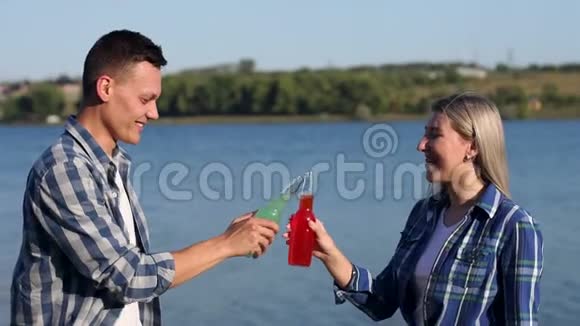 一对夫妇在河岸上休息喝着一瓶低度酒视频的预览图