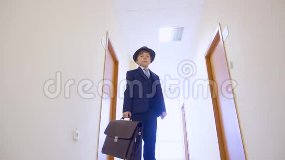 穿着商务服的小男孩帽子站在学校走廊里看着摄像机低角度观看年轻商人视频的预览图