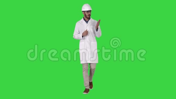 穿着白色长袍和头盔的科学家用手指着侧面在绿色屏幕上向摄像机解释视频的预览图