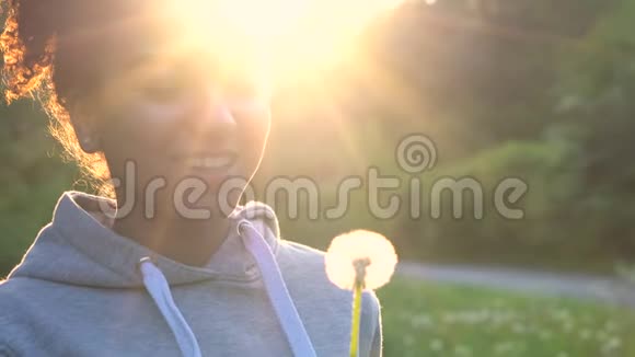 非裔美国少女或年轻女子在日落或日出时笑着吹蒲公英视频的预览图