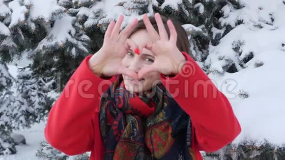 一个年轻的白种人迷人的女孩穿着红色外套在冬天直视镜头和摆姿势的肖像显示了一颗巨大的心视频的预览图