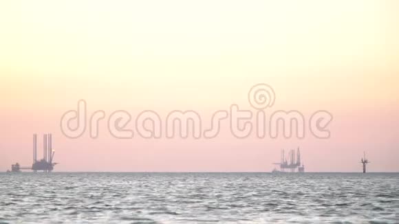 远处两个大型石油钻井平台的剪影海边日落视频的预览图