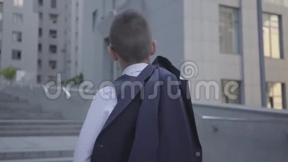 一个英俊的穿着考究的男孩站在街上看着大楼肩膀上戴着夹克严重视频的预览图