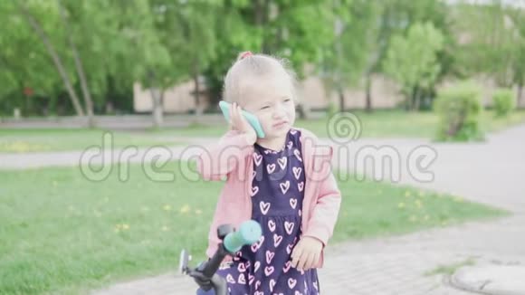 一个小女孩坐在自行车上用玩具手机说话视频的预览图