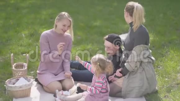 两个母亲和他们的孩子在公园的毯子上一个金发大男孩躺在毯子上一个可爱的小女孩在里面视频的预览图