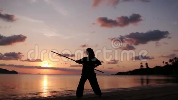 一位年轻有权势的女人用一根功夫棍子站在海滩上的剪影视频的预览图