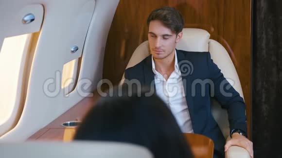 穿西装的年轻商人坐在头等舱的飞机上可敬的有钱人穿着西装坐私人飞机飞行视频的预览图