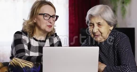 一位戴眼镜的老妇人和一位长着皱纹的祖母正在看笔记本电脑上的照片视频的预览图