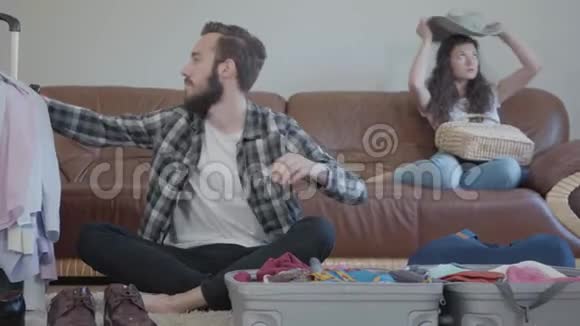 一个穿格子衬衫的大胡子年轻人正把衣服装在旅行箱里可爱的女孩坐在靠近她的沙发上视频的预览图