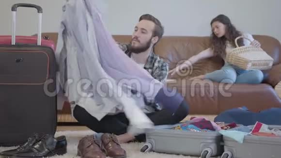 英俊而积极的胡子男人漫不经心地把东西塞进手提箱得意洋洋地举起双手年轻妻子视频的预览图