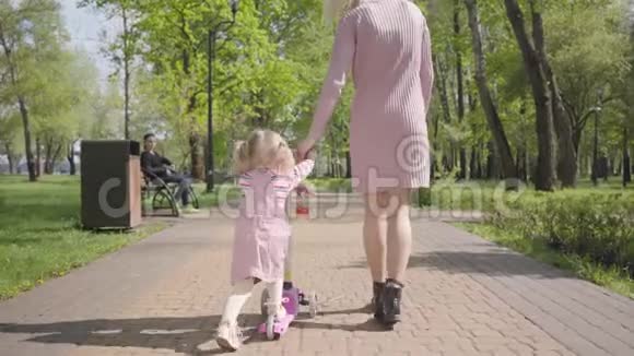 年轻的母亲带着她女儿的滑板车在公园里后景孩子转过头来视频的预览图