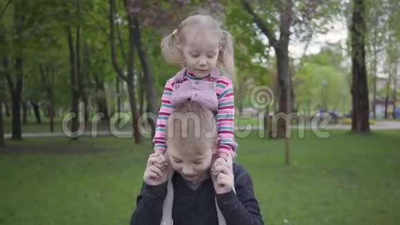 肖像英俊的金发男孩在公园里和她可爱的妹妹玩耍把她抱在肩膀上那个男孩试图视频的预览图
