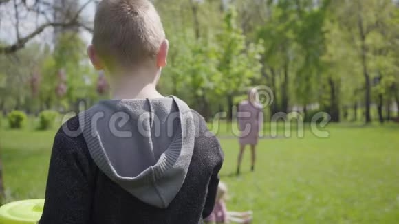 十几岁的金发男孩和他的母亲在公园玩飞盘小孩扔玩具但女人抓不到视频的预览图