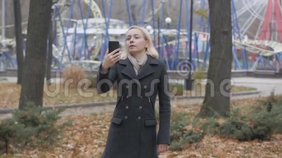 在一个荒芜的秋天公园里一位女博主用智能手机在视频聊天上聊天视频的预览图
