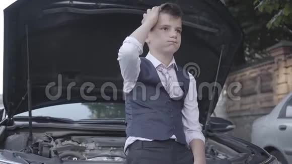 一个穿着西装的小男孩坐在一辆破车的引擎盖旁边心烦意乱孩子长大了视频的预览图