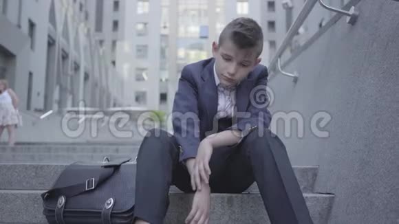 穿着西装的可爱男孩坐在街上的楼梯上这个男孩很累只想成为一个视频的预览图