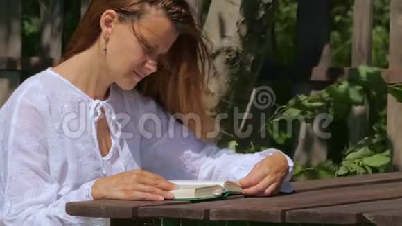 一位年轻女子坐在公园的木桌旁看书视频的预览图
