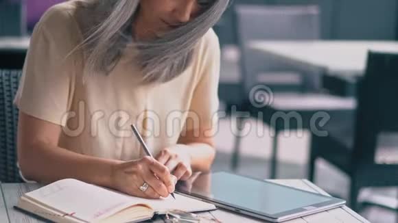 中饱眼福的亚洲女人坐在咖啡馆里在她的笔记本上做笔记视频的预览图