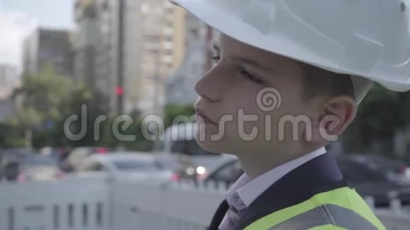 穿着商务服安全装备和建筑工人头盔的可爱的泼辣小男孩站在繁忙的道路上视频的预览图