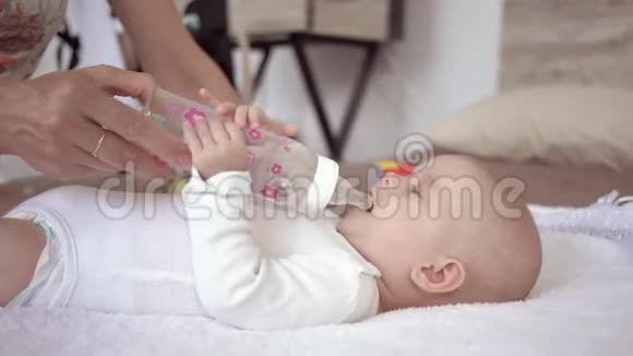 妈妈照顾刚出生的小女孩躺在床上用妈妈手里的一个瓶子喝水视频的预览图