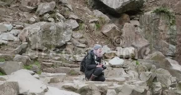 当雪猴围着她跑来跑去时一个女人拿着相机蹲在岩石上视频的预览图