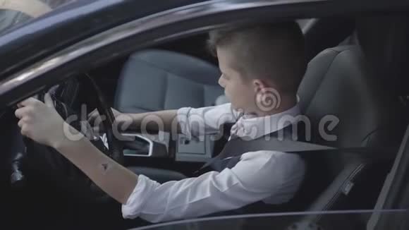 年轻的穿着考究的男孩学习驾驶汽车坐在司机座位特写现代小孩父亲的儿子视频的预览图