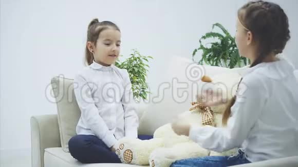 两个漂亮的女孩坐在沙发上玩石头剪刀决定谁来玩白色软熊视频的预览图
