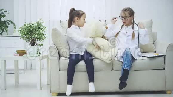 两个可爱的孩子在玩泰迪熊扮演医生的女孩正在用听诊器检查毛绒熊视频的预览图