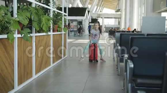 快乐的小女孩在机场大厅里骑着一个红色的大箱子视频的预览图