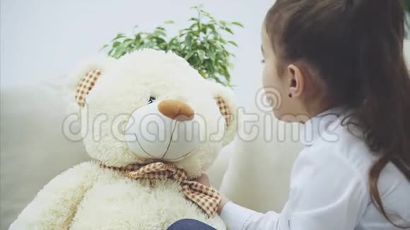可爱的小女孩坐在沙发上和她的泰迪说话在它耳边低语一些秘密视频的预览图