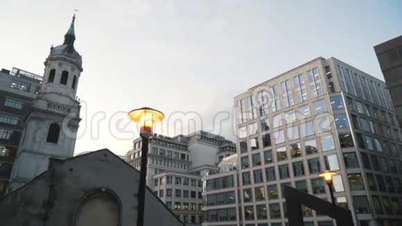 在伦敦市中心在蓝色的夜空下现代化的玻璃摩天大楼附近亮起黄色的路灯视频的预览图