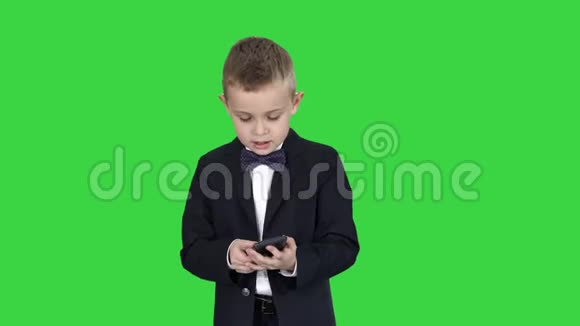 穿着服装走路和使用智能手机的小男孩在绿色屏幕上Chroma键视频的预览图