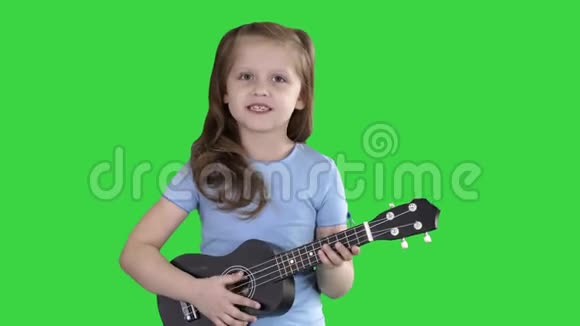 小女孩一边唱着小吉他一边走向绿色屏幕上的相机Chroma键视频的预览图