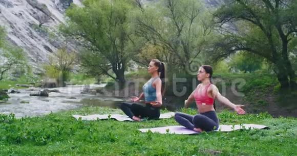两位女士集中在大自然中在美丽的风景中做瑜伽冥想她们集中在一起视频的预览图