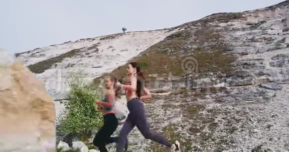 在一个阳光明媚的日子里两位迷人的女士穿过石头路在山中央锻炼身体视频的预览图