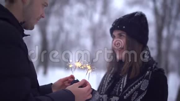 一幅可爱的女孩和一个在白雪覆盖的公园里拿着火花的家伙的肖像恋爱中快乐的一对享受在一起的时光日期视频的预览图